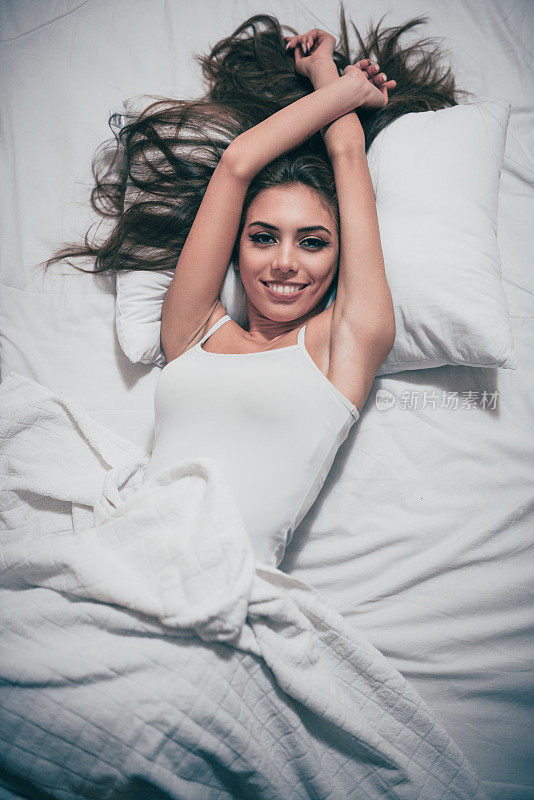 年轻的微笑女性躺在她的卧室和醒来