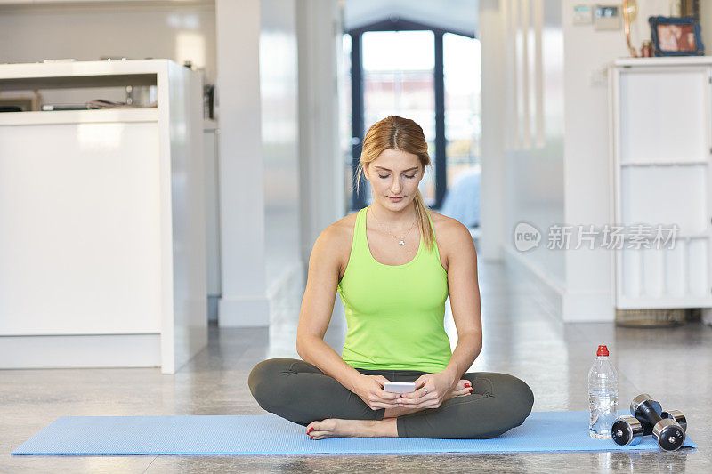 健康女性坐在运动垫上，拿着手机