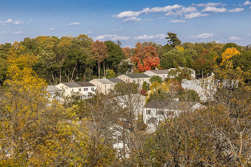 房子之间的树在秋天的颜色(树叶)和蓝天，波基普西，哈德逊山谷，纽约。