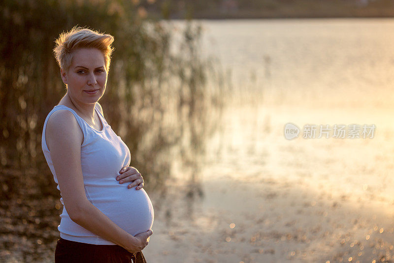 怀孕。怀孕的女人。夕阳在背景中。在水中。