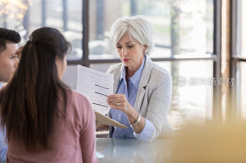 一位年长的女士一边翻阅笔记，一边和一对年轻夫妇交谈