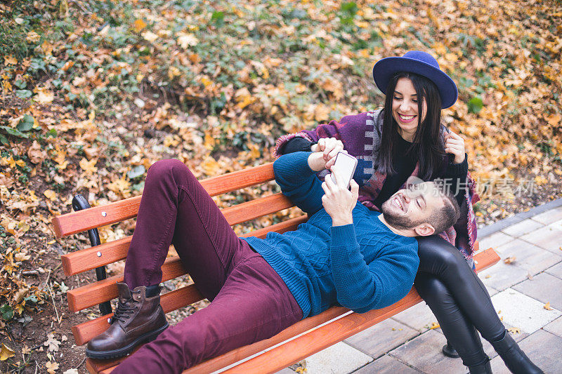 一对可爱的情侣在秋天的公园长椅上自拍