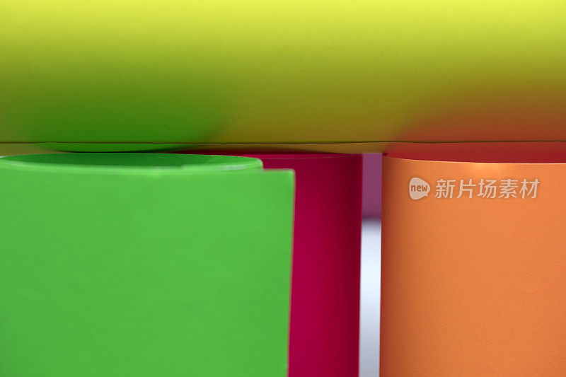 绿色、橙色、黄色和粉色纸张在灰色背景上卷曲。