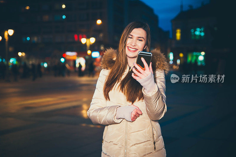 年轻女子晚上在城市里使用智能手机