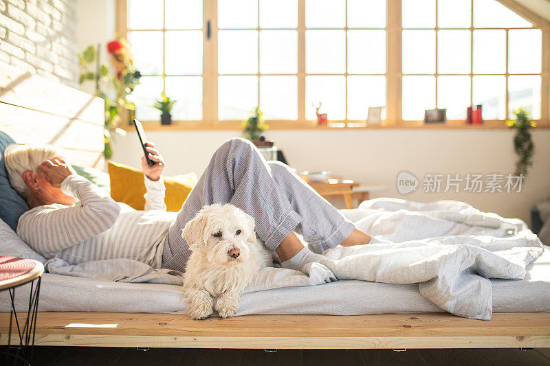 一名退休妇女在床上和狗玩智能手机