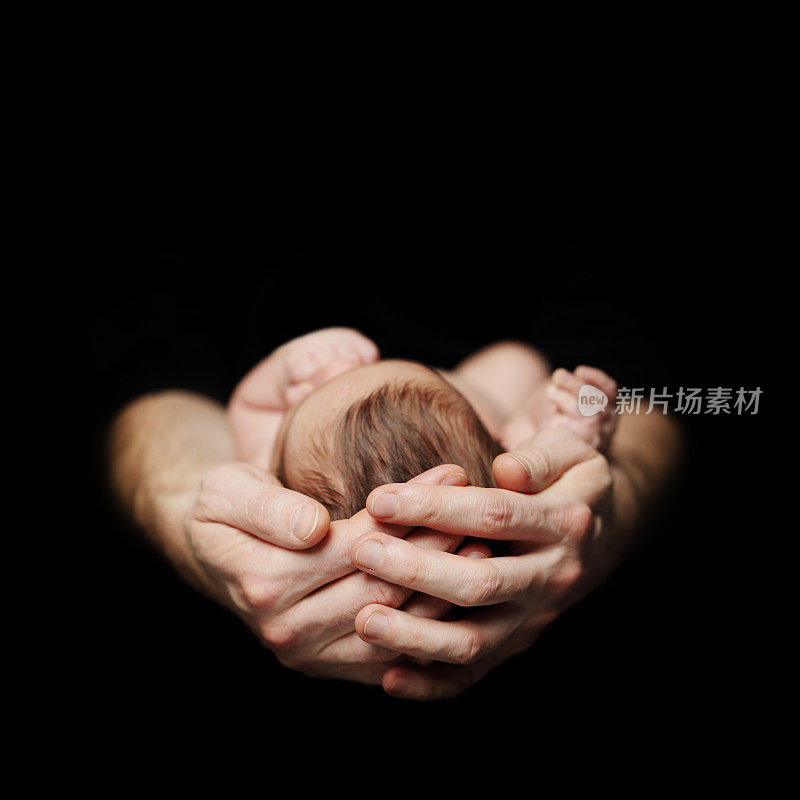 亲子关系的概念。黑色背景上的新生儿在父亲的手上