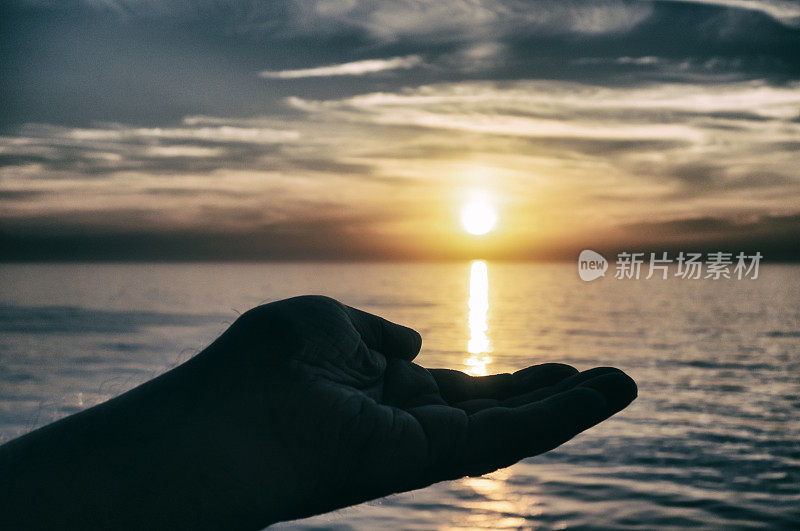 神秘男子的剪影手捧着海上的夕阳