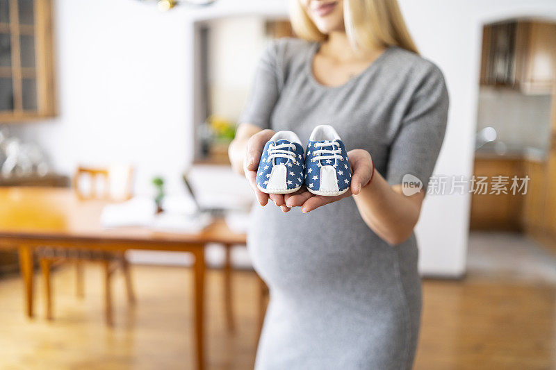 孕妇站着，手里拿着可爱的婴儿鞋