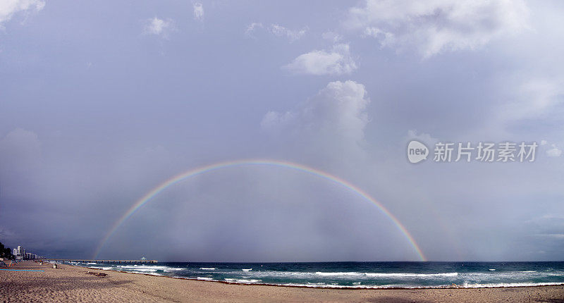 有沙滩和钓鱼码头的海景在雨天的天空和彩虹