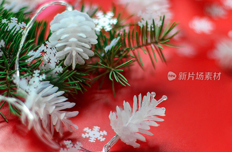 由红色背景上的白色松果和圣诞树的树枝组成的圣诞花环。选择性聚焦，侧视图，拷贝空间。