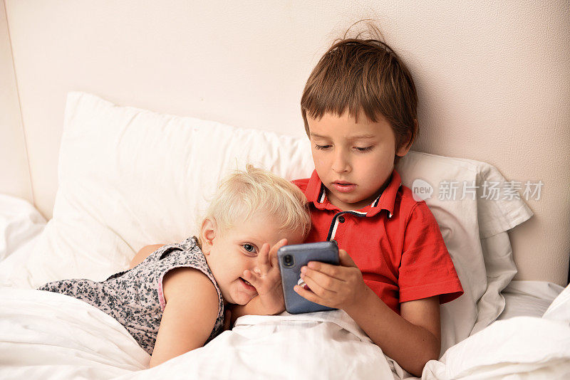 孩子们在床上用智能手机看电影。