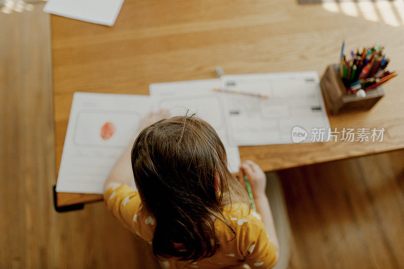 2019冠状病毒病期间，身着黄色连衣裙的幼儿园学生坐在餐桌前做作业