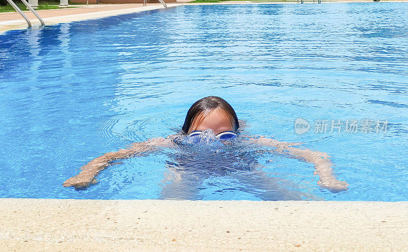 一个白人女孩，7岁，在室外游泳池游泳，在水里挣扎。夏天晴朗的一天。