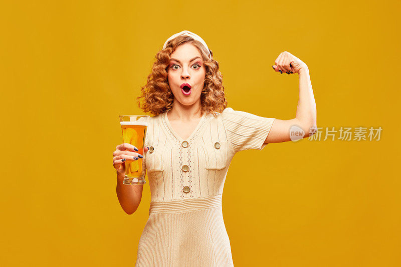 年轻女子穿着复古的连衣裙，拿着大啤酒杯，在黄色的背景下展示着力量。酒花的力量