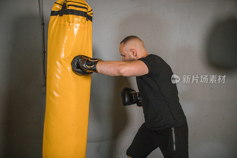 专注的男战士独自在健身房训练，打一个沙袋。在健身房打拳击——健康生活方式的概念