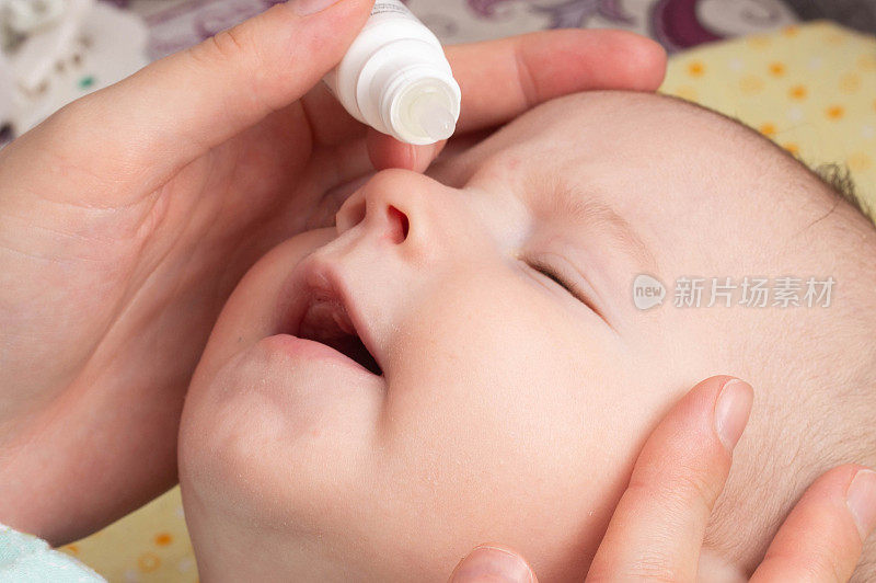 一位母亲在孩子的眼睛里滴药来治疗脓和眼泪。含维生素的眼药水，特写