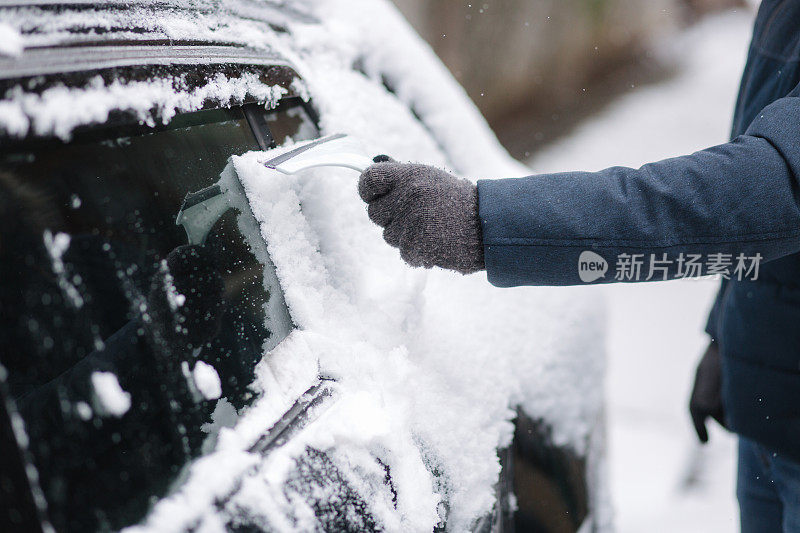 一名男子正在用刮雪机清理汽车上被雪覆盖的窗户。关注刮刀。寒冷的雪和霜的早晨。黑色的车