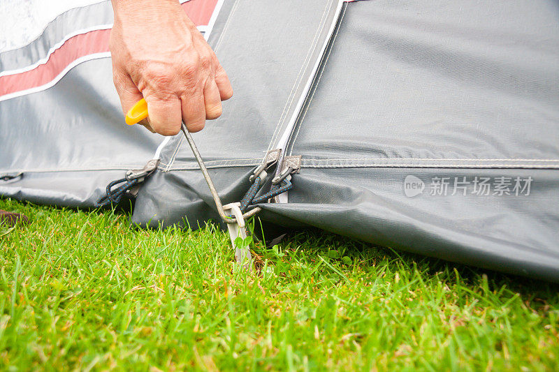 近距离拍摄的男子用钩子工具拔出帐篷的挂钩，帐篷的挂钩被用来固定帐篷的位置，为度假的家庭提供更多的空间。