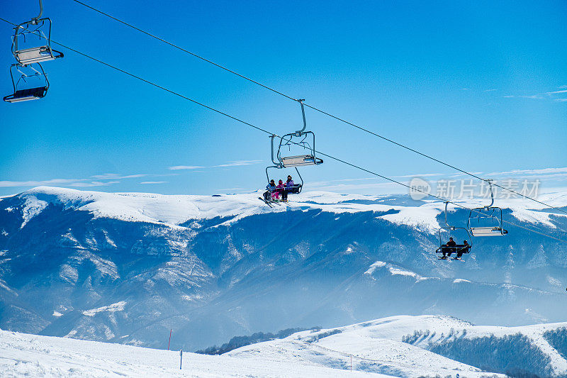 在一个晴朗的日子里，滑雪缆车在白雪皑皑的山峰和山坡上移动