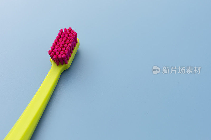 平铺模型绿色牙刷与粉红色刷毛躺在蓝色背景，复制空间为特克斯。早上卫生，浴室用品。牙科保健模板。水平顶视图