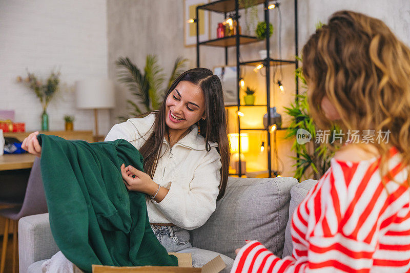 两个女性朋友在家里打开一包衣服的盒子