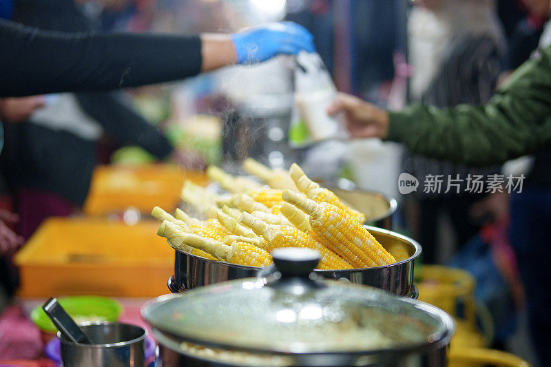 一个特写镜头，在一个亚洲夜市，一个金属蒸笼托盘上的蒸玉米，准备出售食物。