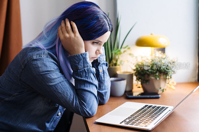 迷人的年轻拉丁裔女孩的肖像，蓝头发，蓝色牛仔衬衫，坐在咖啡馆里，在笔记本电脑上工作，有复印空间。