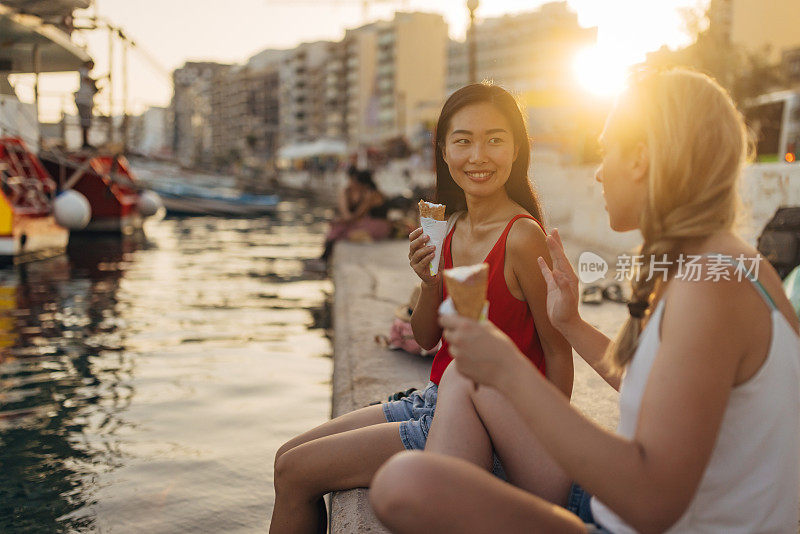 两个女人坐在码头上享受一个阳光明媚的夏日，吃着甜筒冰淇淋