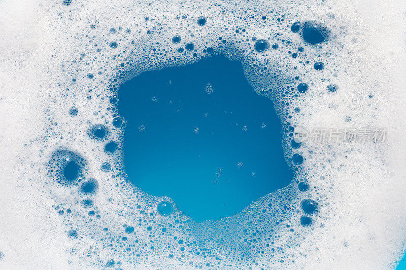 洗涤剂在水中起泡沫。蓝色背景，肥皂色