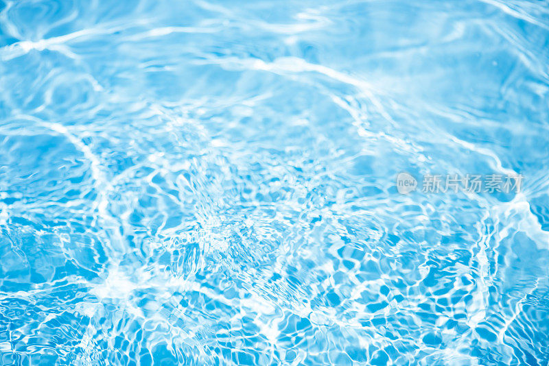 蓝水的波浪在水面上泛起模糊的涟漪。散焦模糊透明蓝色透明平静水面纹理与飞溅和泡沫。水波与闪亮的图案纹理背景。