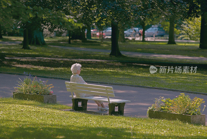 孤独的白发老人躺在公园的长椅上晒太阳