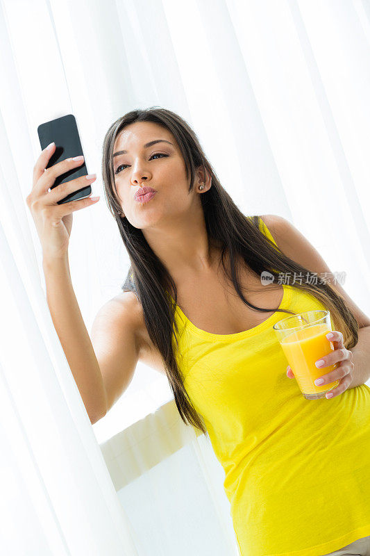 年轻女子喝着橙汁自拍，亲吻