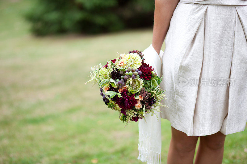 新娘身穿短裙，手捧花束在草地上