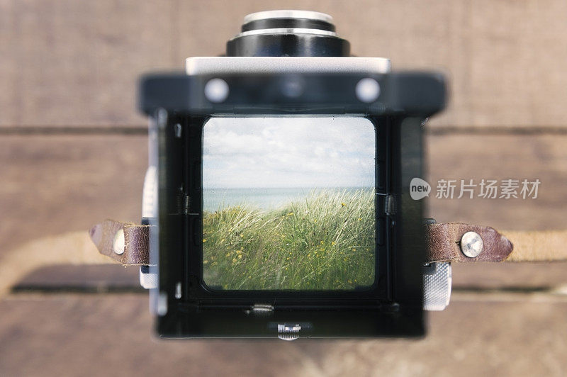透过古董相机的取景器，可以看到沙丘之外的大海和天空
