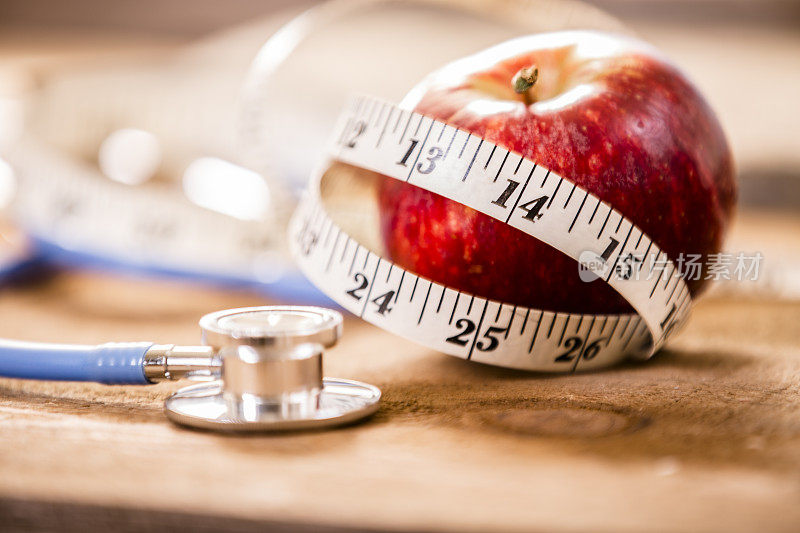 健康的苹果与医生的听诊器和卷尺。