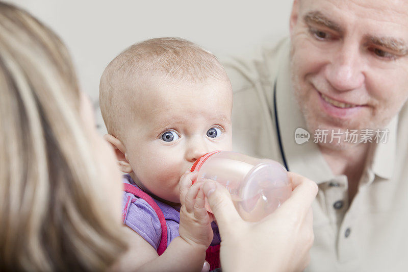父亲看着母亲用奶瓶喂女婴