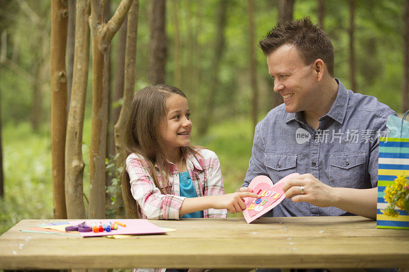 女儿给爸爸看手工制作的父亲节卡片。在户外。孩子,父母。