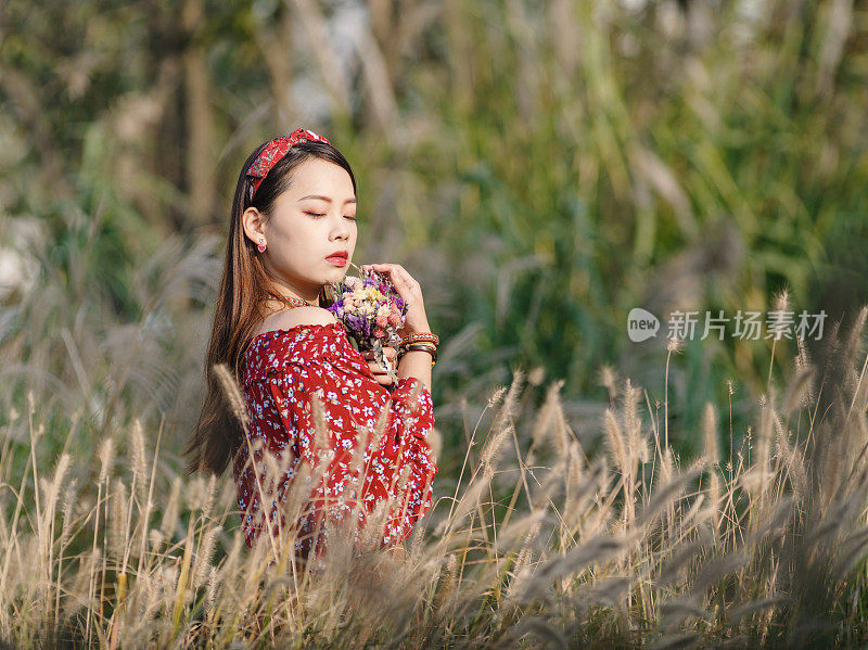 一个美丽的中国女孩的肖像站在黄色的芦苇田在阳光明媚的秋日。