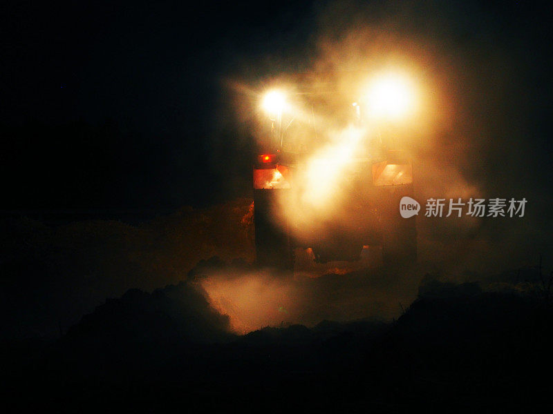 拖拉机在夜晚的大雾中工作，车头灯。农业机械。收成。拖拉机在晚上准备土地