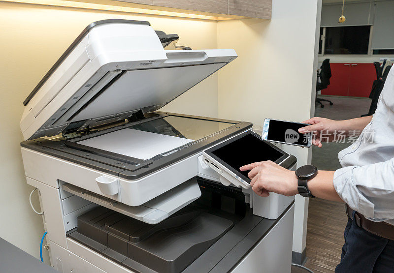 一名男子用智能手机用近场通信技术从复印机上复印纸张