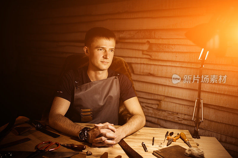 皮带在皮革车间的工作过程。男人在木桌上牵着手。制作工具的背景。旧制革厂的皮匠。用于文本和设计的暖光。网络横幅尺寸