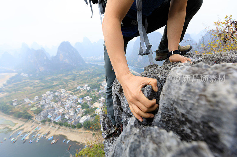 勇敢的女子背包客攀登岩石在山顶悬崖边缘