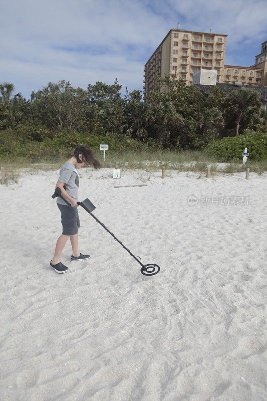 海滩上拿着金属探测器的男孩。