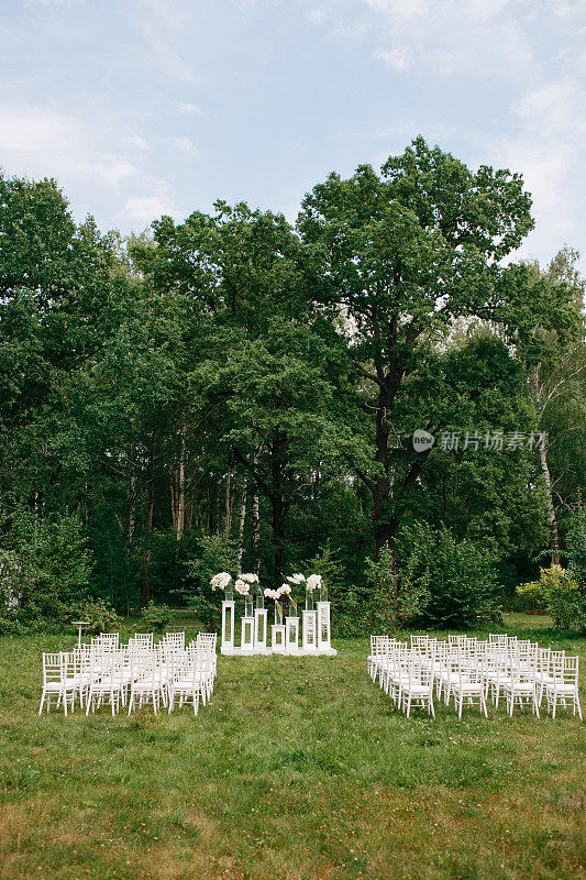 婚礼在一个美丽的花园里举行。白色的椅子和镜面的桌子。玻璃花瓶上有马蹄莲、孤挺花