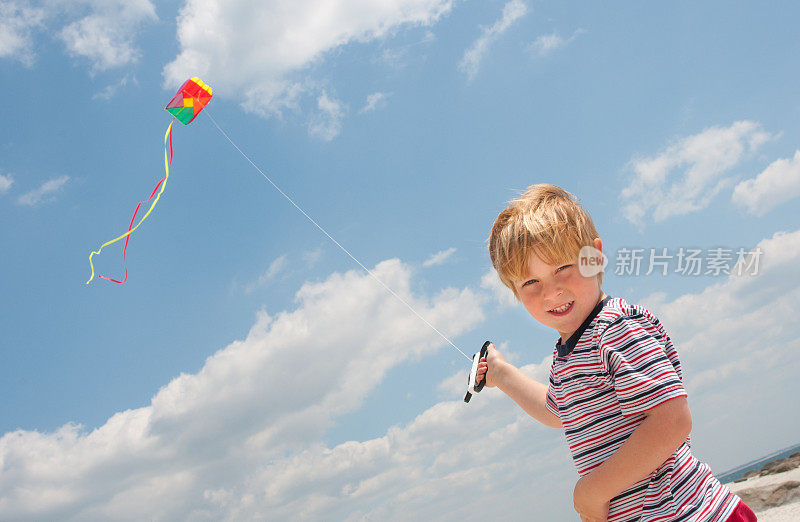 快乐的5岁男孩在一个阳光明媚的日子里，穿着T恤跑着放五颜六色的风筝