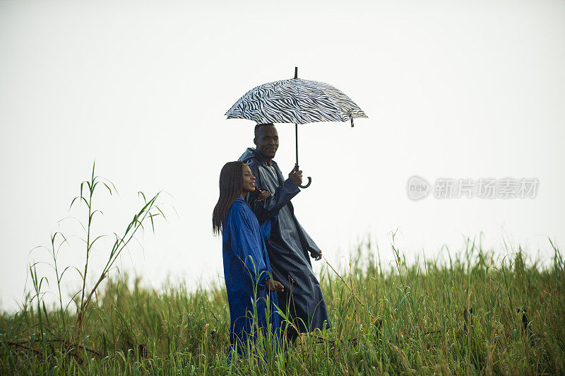 侧视图的幸福夫妇一起走在雨中与雨衣和雨伞
