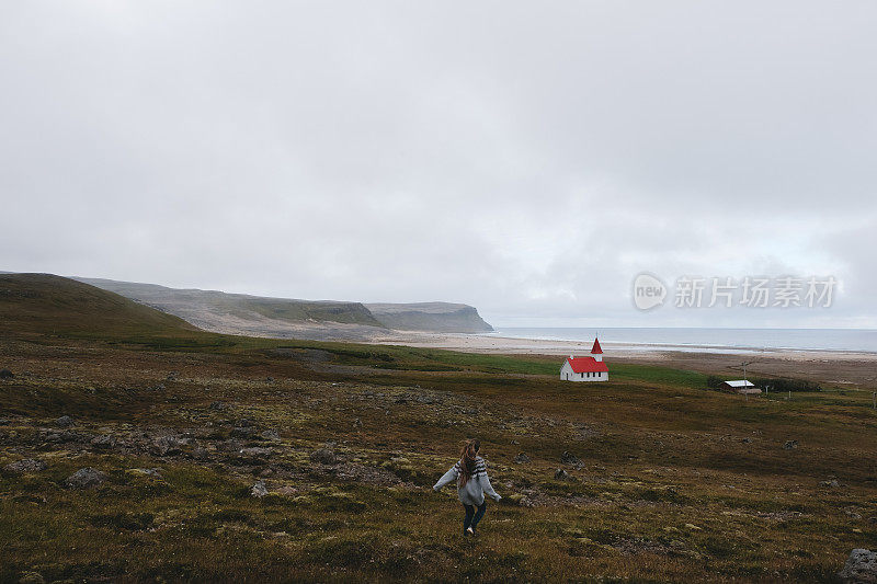 穿着羊毛衫的女人跑到遥远的美丽的教堂附近的海洋和山脉在冰岛