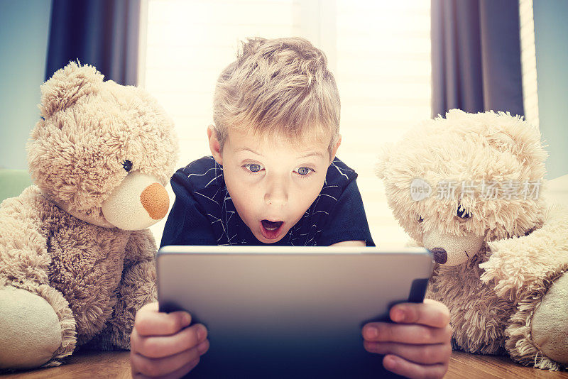 一个微笑的男孩和一只泰迪熊正在用平板电脑看电影
