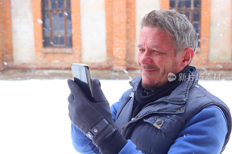 英俊快乐的成年人在下雪的冬天在城市街道上使用手机