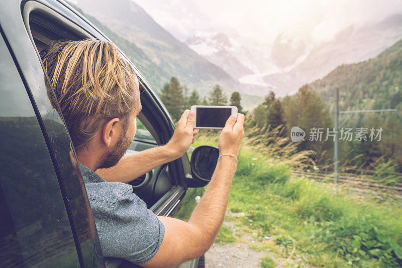 年轻人在路边的车里用手机拍风景。用智能手机拍摄美丽的山脉和冰川风景